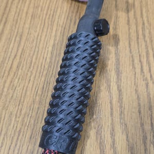 Op de afbeelding: Een zwarte TIG-lastoorts met een getextureerde handgreep en een rood-zwart patroon kabel. De toortskop is zwart en wit met een roze keramische nozzle.
