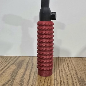 Op de afbeelding: Een TIG-lastoorts met een rode, getextureerde handgreep, zwarte behuizing en een roze keramische nozzle. De toorts heeft een zwarte knop en een punt. De achtergrond is licht.