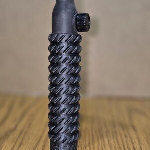 May include: A black TIG welding torch with a textured handle. The torch has a pink ceramic nozzle, a black body, and a knurled adjustment knob. The handle has a ridged design for grip.