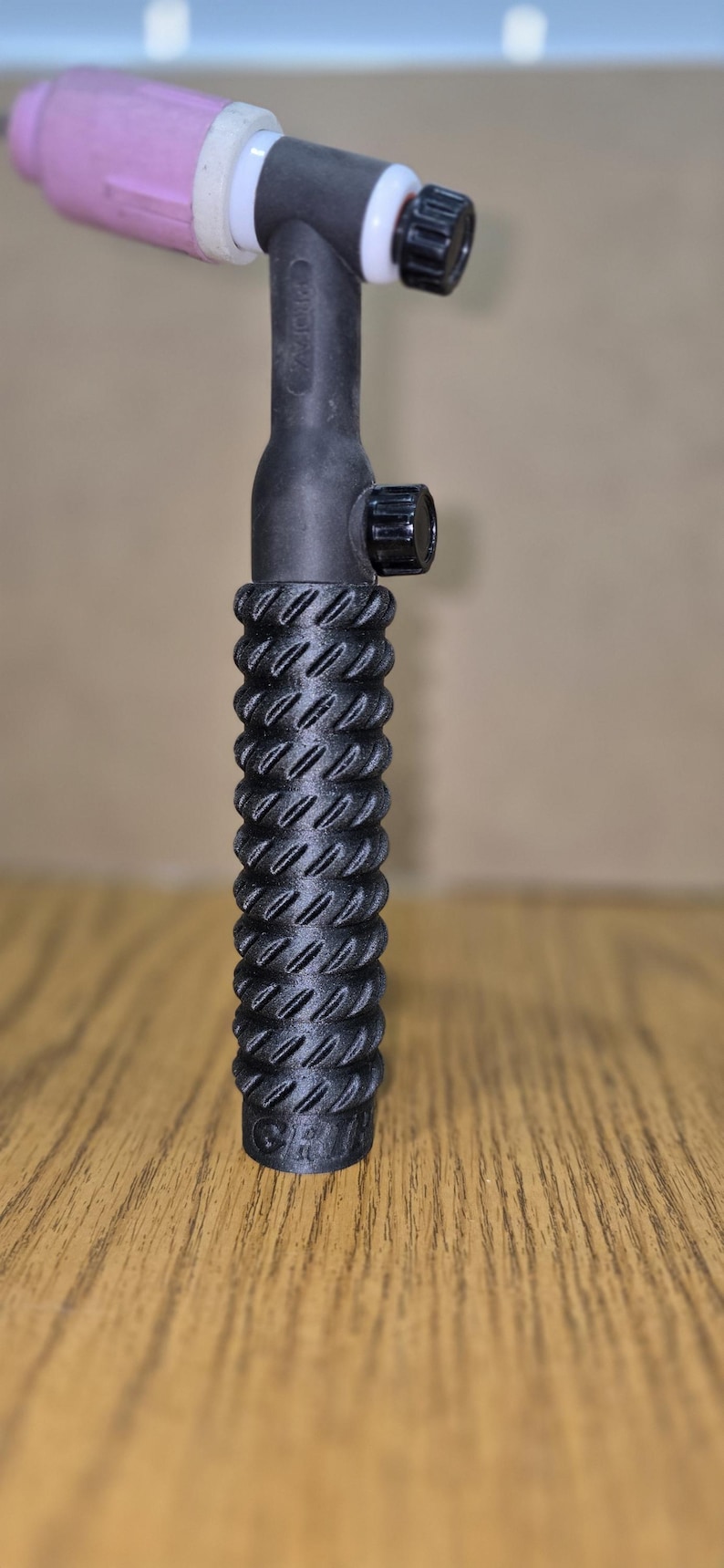 May include: A black TIG welding torch with a textured handle. The torch has a pink ceramic nozzle, a black body, and a knurled adjustment knob. The handle has a ridged design for grip.