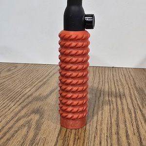Op de afbeelding: Een TIG-lastoorts met een roze keramische nozzle, zwarte behuizing en een oranje, getextureerde handgreep. De toorts is ontworpen voor precisielassen en staat tegen een witte achtergrond en houten oppervlak.