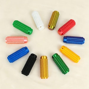 Puede incluir: Una colección de diez objetos cilíndricos coloridos con superficies texturizadas. Los objetos están dispuestos en un patrón circular y vienen en varios colores, incluyendo verde, blanco, dorado, rojo, azul, negro y amarillo.