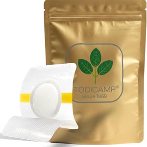 May include: A clear medical product with a white absorbent pad and yellow accents is displayed in front of a gold-colored pouch. The pouch features a green leaf design and the text "TODICAMP® Since 1969".