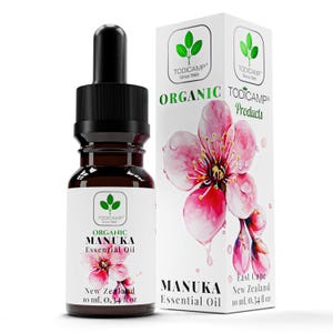May include: A dark amber glass bottle with a black dropper and a white label featuring the text "Organic Manuka Essential Oil." A matching box displays a pink flower illustration and the brand name "Todicamp."