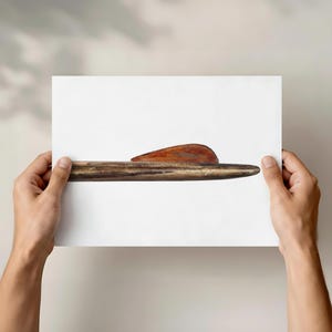 May include: A wooden object with a pointed end and a curved, reddish-brown piece on top. The object is held against a white background, showcasing its natural wood grain and texture. The overall aesthetic is minimalist and earthy.