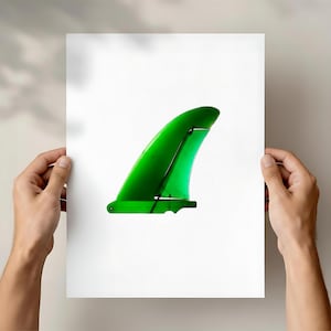 May include: A translucent green surfboard fin, set against a white backdrop. The fin has a curved design and is held up by two hands. The fin's colour is a vivid green.