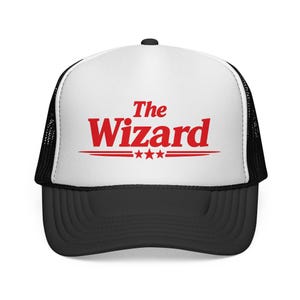 May include: A black and white trucker hat with a white front panel. The front of the hat features the red text "The Wizard" above three red stars and two red lines. The brim is black.