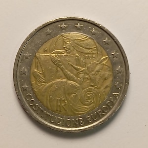 Può includere: Una moneta da due euro con un centro dorato e un anello esterno argentato. Il centro dorato raffigura una donna che legge, con l'anno 2005 visibile. Il bordo della moneta presenta stelle e la scritta "COSTITUZIONE EUROPEA".