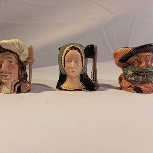 Puede incluir: Tres tazas de cerámica con forma de personajes. Las tazas tienen forma de figuras históricas, como un hombre con bigote y sombrero, una mujer con cofia y un hombre barbudo con sombrero. Las tazas están pintadas en varios colores.