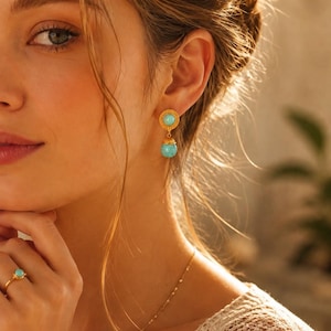 May include: A gold earring featuring a circular stud with a central turquoise stone and a dangling turquoise bead, paired with a matching gold ring set with a single turquoise stone. The jewellery pieces are crafted with a polished gold finish.