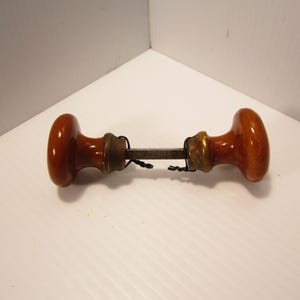 May include: A pair of brown ceramic door knobs with a metal connecting rod. The knobs are attached to the rod with brass accents.