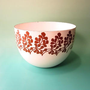 May include: White bowl with a brown floral design around the rim. The bowl has a rounded shape and is set against a light blue-green background. The floral pattern is a repeating design of leaves and stems.