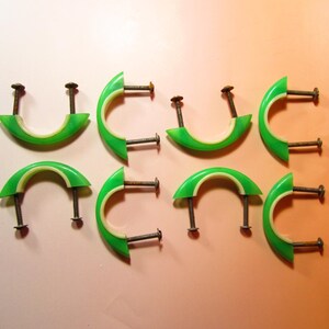 May include: Eight green and white cabinet pulls with metal screws. The pulls have a curved, half-circle design with a bright green exterior and a white interior. The screws are dark brown.