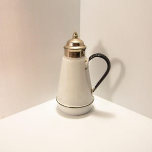 May include: White enamel pitcher with a black handle and a silver lid. The pitcher has a conical shape and a small spout.