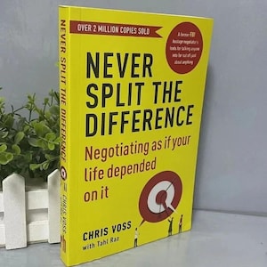 Könnte beinhalten: Ein gelbes Buch mit dem Titel "Never Split the Difference" mit schwarzem Text. Das Buchcover enthält den Text "Negotiating as if your life depended on it" und "Over 2 million copies sold."