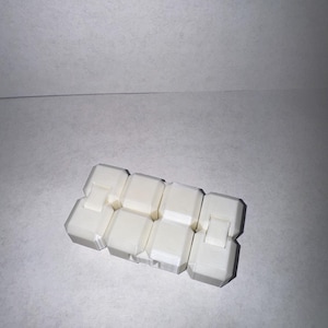 May include: A white, articulated fidget toy composed of several connected rectangular blocks. The blocks are arranged in a zig-zag pattern, allowing for flexible movement and manipulation. The toy is designed to provide tactile stimulation and stress relief.