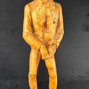 May include: A carved wooden figurine of a man wearing a hat and holding a wine glass. The figure has a long beard and is dressed in a suit. The statue is standing on a wooden base and is made of light brown wood.