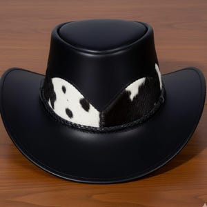 Pu&ograve; includere: Cappello da cowboy in pelle nera con fascia in pelle di mucca con macchie bianche e nere. Il cappello ha una tesa classica e un bordo intrecciato attorno alla fascia. Il cappello &egrave; esposto su una superficie di legno.