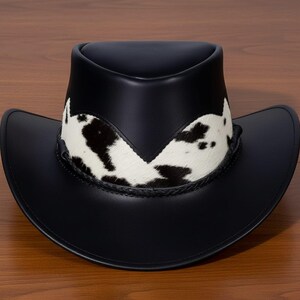Pu&ograve; includere: Cappello da cowboy in pelle nera con fascia in pelle di mucca con macchie bianche e nere. Il cappello ha un'ampia tesa e un classico design western.