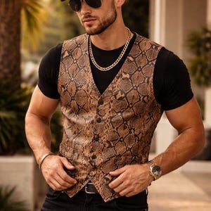 Puede incluir: Un chaleco marrón con estampado de piel de serpiente y una gorra de béisbol a juego. El chaleco tiene una parte delantera abotonada y se lleva sobre una camiseta negra. La persona también lleva vaqueros negros, gafas de sol y una cadena de oro.