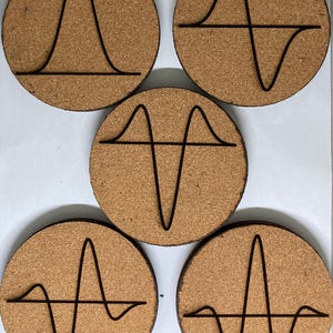May include: Five round cork coasters with black line art designs. Each coaster features a different abstract wave or graph pattern. The coasters are a natural brown color, and the designs are simple and modern.