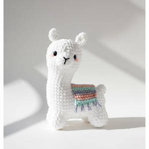 Peut inclure: Un lama amigurumi blanc au crochet avec une couverture colorée. Le lama a de petites oreilles, un nez noir en forme de 'Y' et des joues roses. Le texte en haut indique "Crochet Toy Pattern PDF - Instant Download".