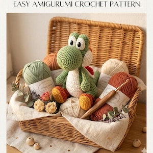 以下が含まれることがあります： 緑、白、オレンジ色の編みぐるみヨッシー人形、毛糸玉、かぎ針編み針が入った柳のバスケット。バスケットにはドライフラワーと「EASY AMIGURUMI CROCHET PATTERN」の文字も含まれています。