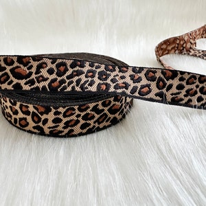 May include: A roll of brown and black leopard print ribbon. The ribbon is woven with a black border.