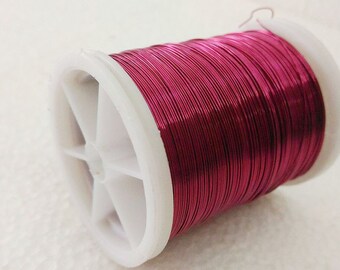 Könnte beinhalten: Eine Spule mit leuchtend pinkfarbenem Metalldraht auf einer weißen Kunststoffspule. Der Draht ist fest um die Spule gewickelt.
