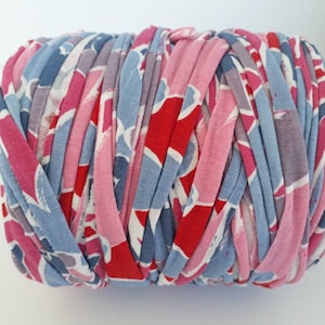 May include: A cylindrical ball of fabric strips in shades of red, pink, and blue. The fabric strips are tightly wound together, creating a textured surface. The fabric has a floral pattern.