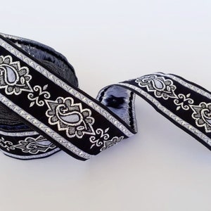 May include: Black and silver trim with a paisley pattern. The trim is rolled up and has a silver metallic thread running through it.