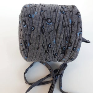 May include: A roll of gray t-shirt yarn with a blue and black print of stars, lightning bolts, and a monster face. The yarn is tied with a bow.