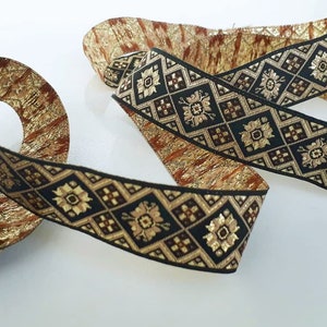 Könnte beinhalten: Goldene und schwarze Borte mit geometrischem Muster. Die Borte hat einen metallischen Glanz und ist mit einem sich wiederholenden Muster aus Quadraten und Blumen gewebt.