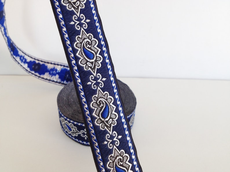 Puede incluir: Borde azul y plateado con un dise&ntilde;o de paisley. El borde est&aacute; enrollado en un carrete.