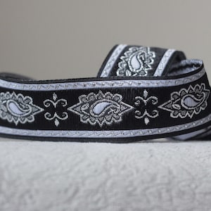 May include: Black and silver trim with a paisley pattern. The trim is woven with a silver thread and has a black background.