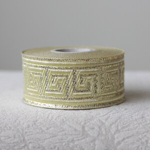 May include: A roll of gold and ivory ribbon with a geometric pattern. The ribbon is approximately 1 inch wide.