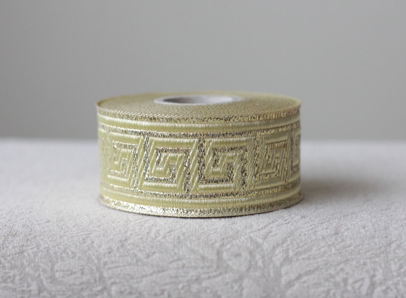 May include: A roll of gold and ivory ribbon with a geometric pattern. The ribbon is approximately 1 inch wide.
