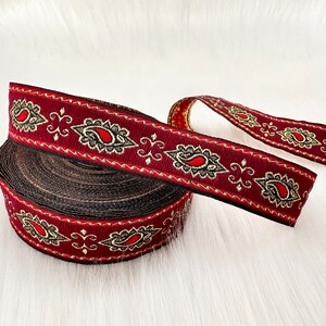 May include: A roll of burgundy trim with a gold and black paisley pattern. The trim is approximately 1 inch wide.