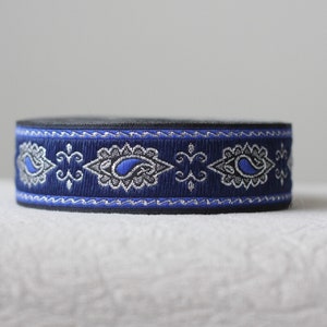 Puede incluir: Cinta de adorno azul y plata con estampado paisley y respaldo negro. La cinta tiene un patr&oacute;n repetitivo de formas paisley y un borde ondulado.