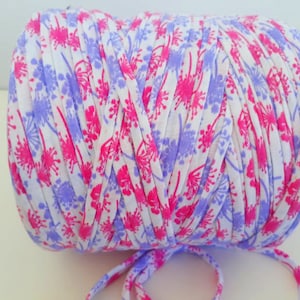 May include: A roll of white, pink, and purple patterned yarn. The yarn is made of cotton and is perfect for crocheting or knitting.
