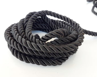 May include: A close-up of black braided cord, twisted and coiled together. The cord is soft and flexible, and it has a subtle sheen.