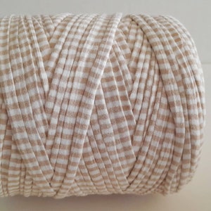May include: A tightly wound ball of beige and white checkered fabric, likely yarn or cord, is displayed against a plain white background. The fabric appears to be soft and textured, suitable for crafting projects. The pattern is a classic gingham check.