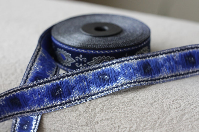 Puede incluir: Borde azul y plateado con un patr&oacute;n decorativo. El borde est&aacute; enrollado en un carrete.