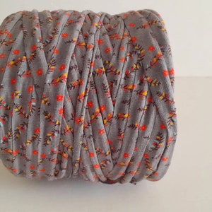 May include: A roll of gray yarn with a floral print featuring orange and yellow flowers. The yarn is tightly wound and ready for crafting.