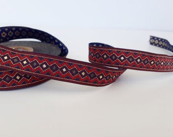 May include: Red, gold, and blue patterned ribbon with a geometric design. The ribbon is woven with a zig-zag pattern and has small diamond shapes.