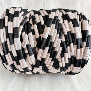 May include: A tightly wound roll of fabric in a black and beige striped pattern. The stripes are evenly spaced and create a visually appealing texture. The material appears soft and pliable, suitable for various craft projects.
