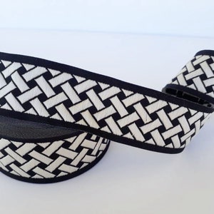 May include: A roll of decorative ribbon with a woven basket weave pattern. The ribbon features a black border and a repeating design of white and black rectangles. The ribbon is ideal for crafts, gift wrapping, and other decorative projects.