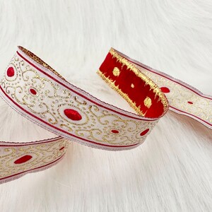 May include: White ribbon with a gold and red design. The ribbon has a repeating pattern of gold swirls and red circles.