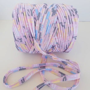 May include: A pink, yellow, blue, and gray yarn with a printed pattern. The yarn is wound into a ball and a length of yarn is hanging off the ball.