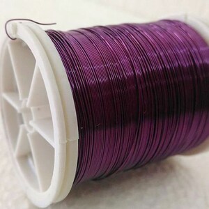 May include: A spool of purple metallic wire on a white plastic spool.